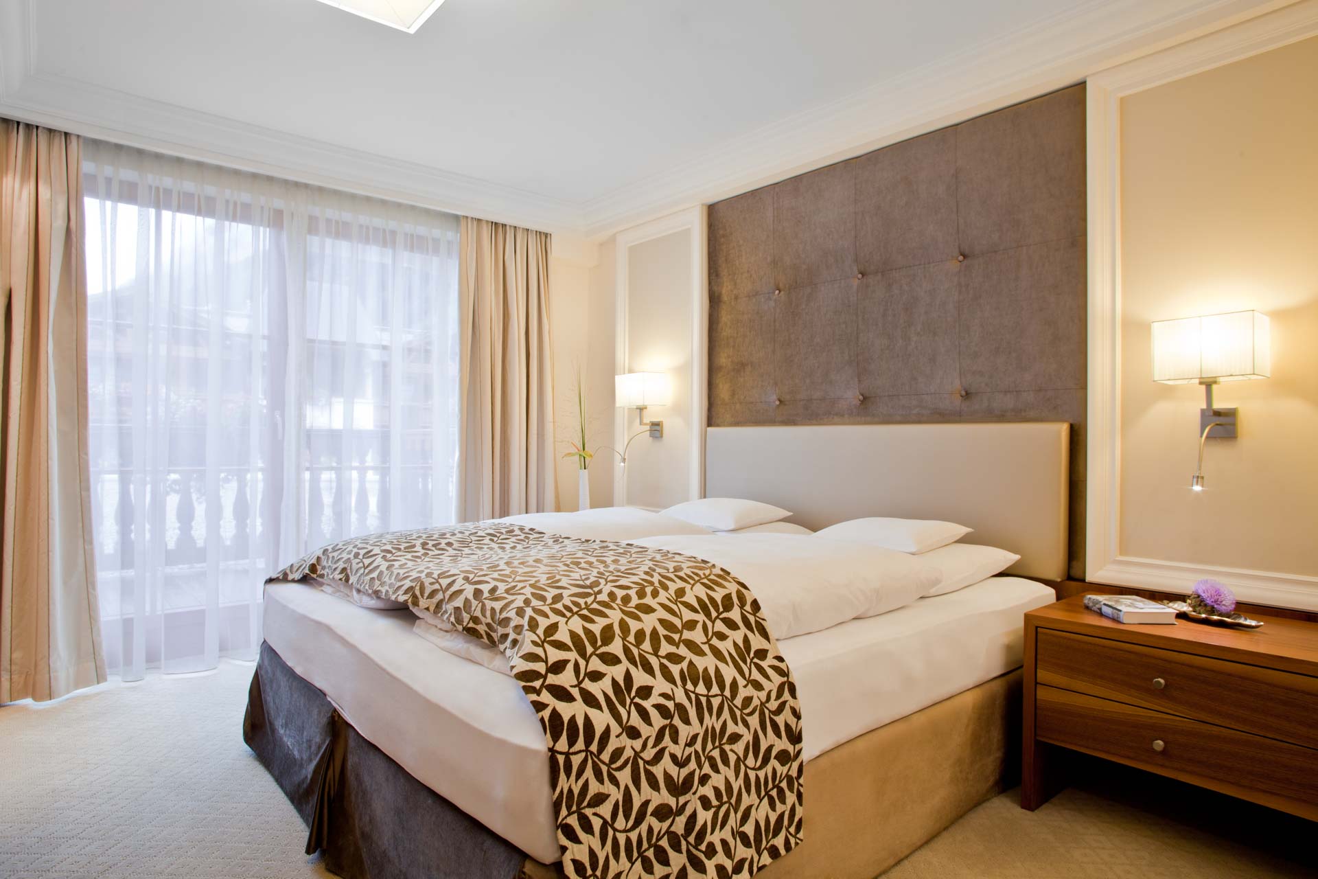 Suite im modernen Stil im Trofana Royal in Ischgl, Detail Bett, Nachttisch, Leuchten und Balkontür